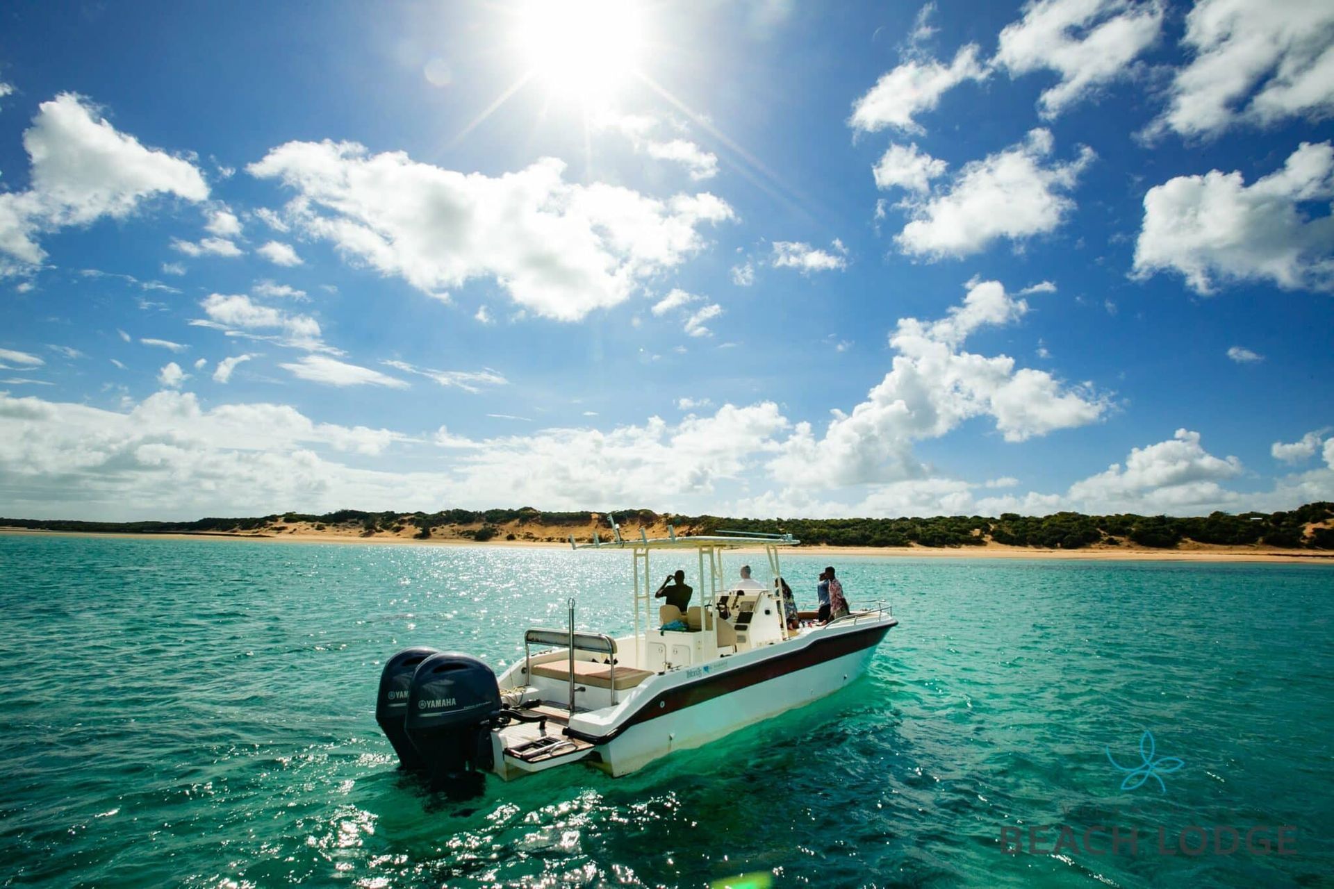 Small motorboat on turquoise water under a bright blue sky with clouds, near a sandy shoreline