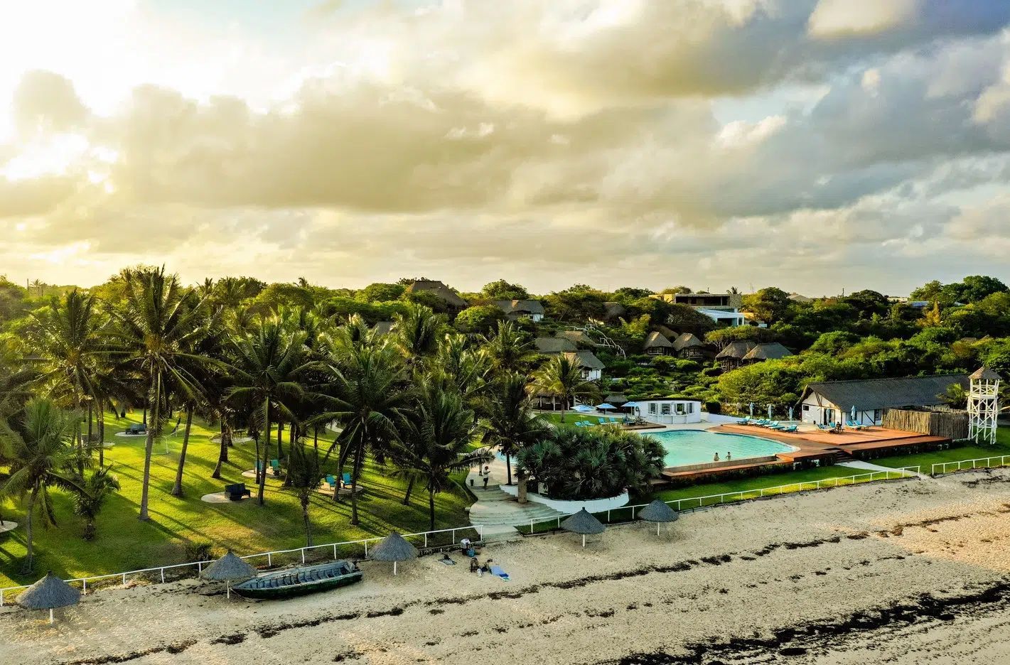 Tropical resort with palm trees, pool, beach, and cloudy sky at sunset