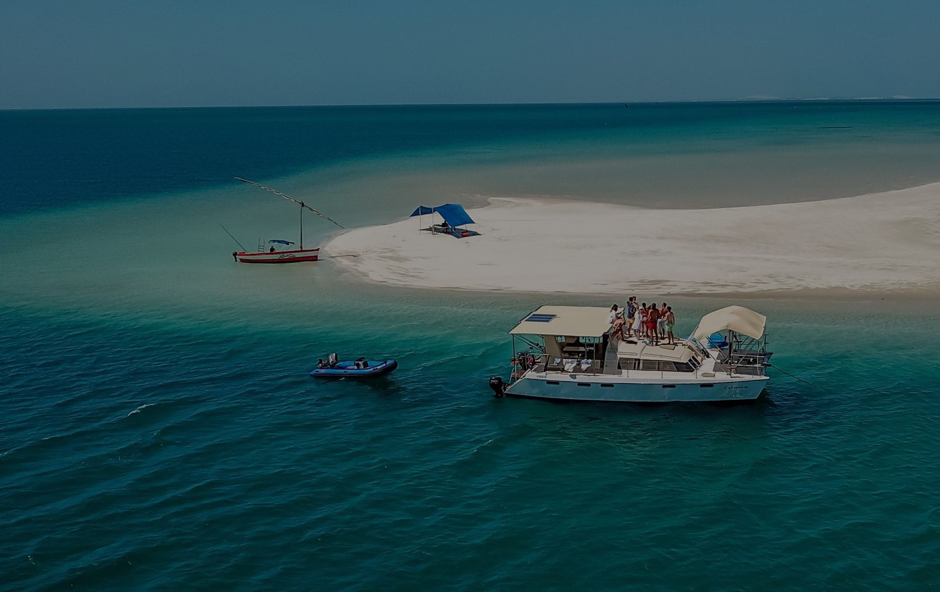 Aerial view of a small sandbar with boats floating in turquoise water.