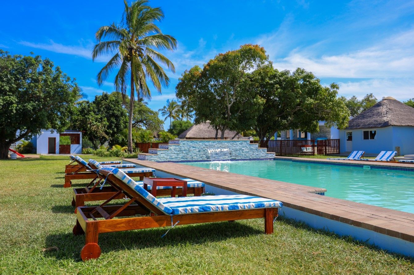 Resort pool with blue lounge chairs, palm trees, and a clear blue sky on a sunny day