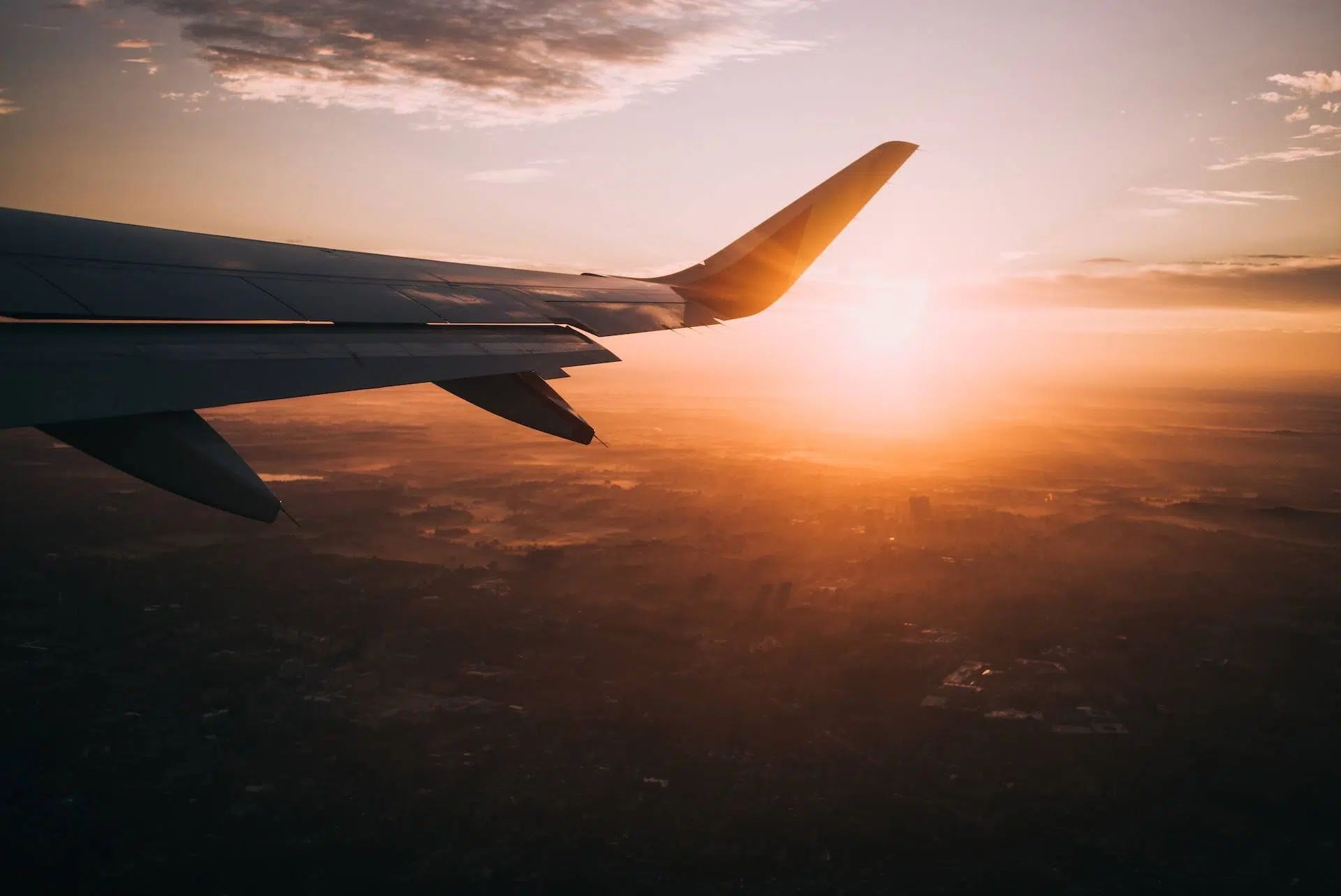 Airplane wing silhouetted against a golden sunset above clouds