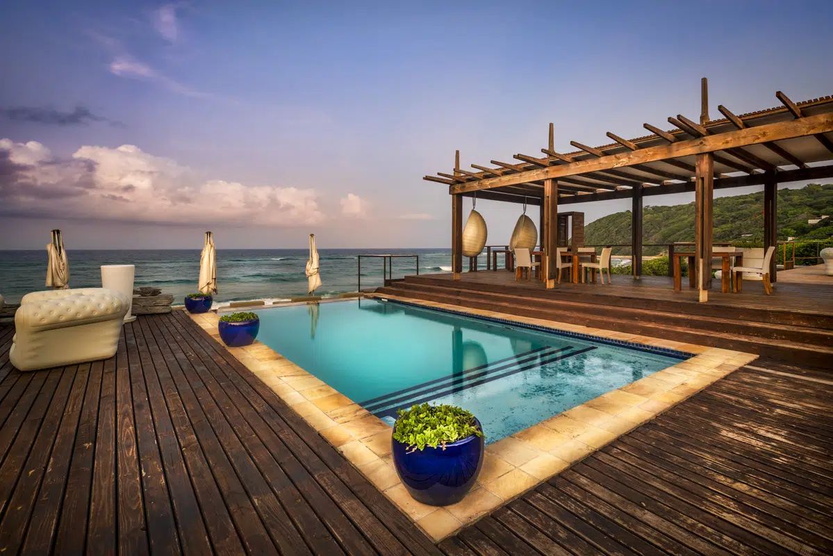 Luxury pool deck by the sea with lounge chairs, wooden pergola, and blue sky at sunset