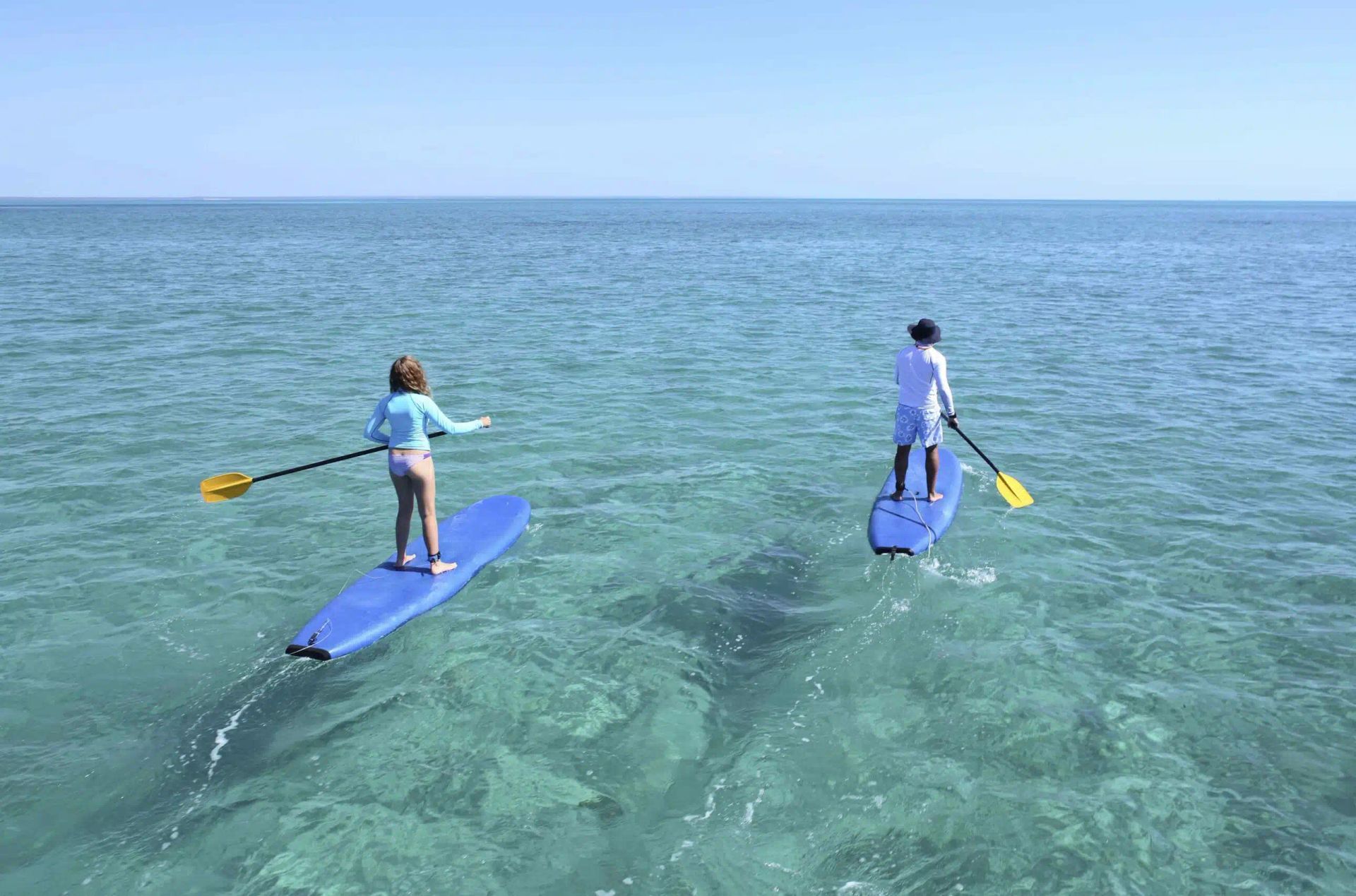 Two people paddleboard on clear blue water near the open sea