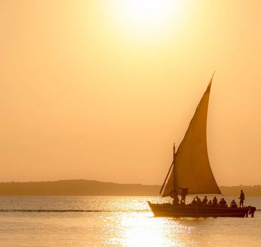 Silhouetted sailboat on calm water at sunset with golden sky and glowing reflections