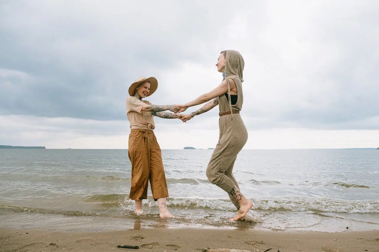Two people holding hands and splashing in shallow water on a cloudy beach