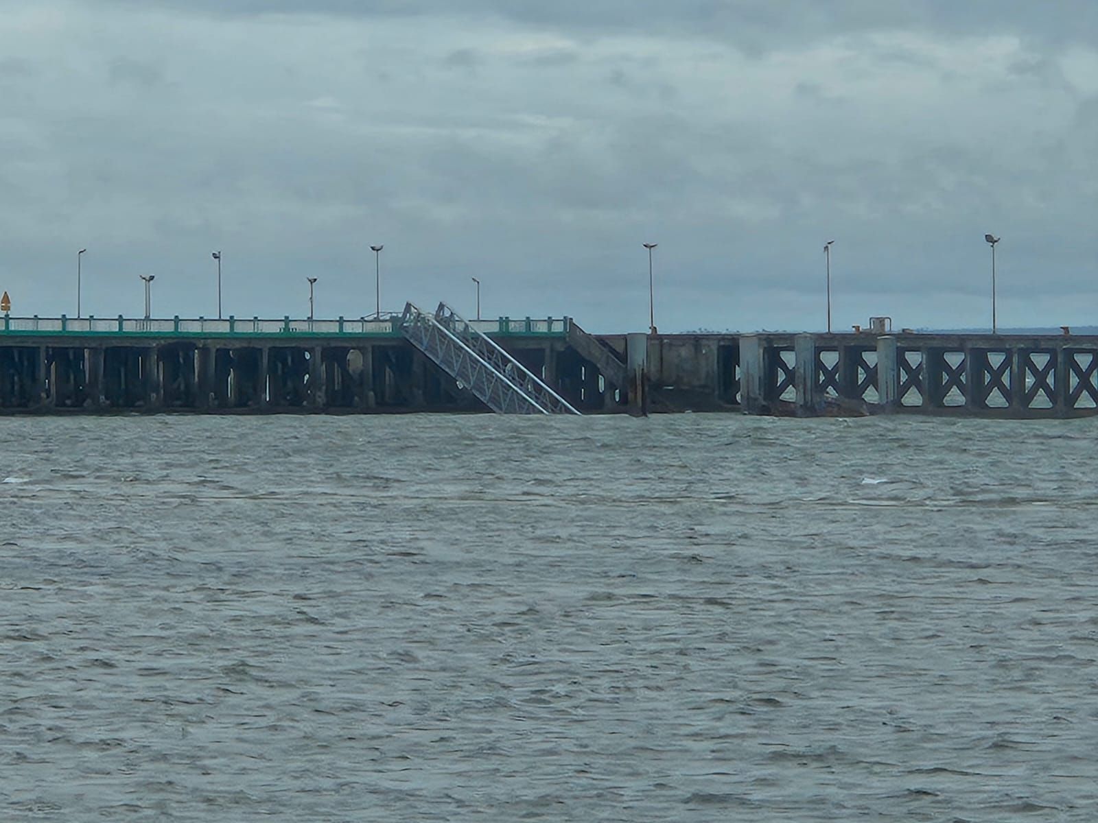 A long pier over choppy water under a cloudy sky, with a staircase descending from the deck.