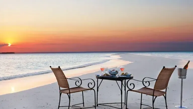 Beachside table and chairs at sunset beside calm ocean, with drinks on the table