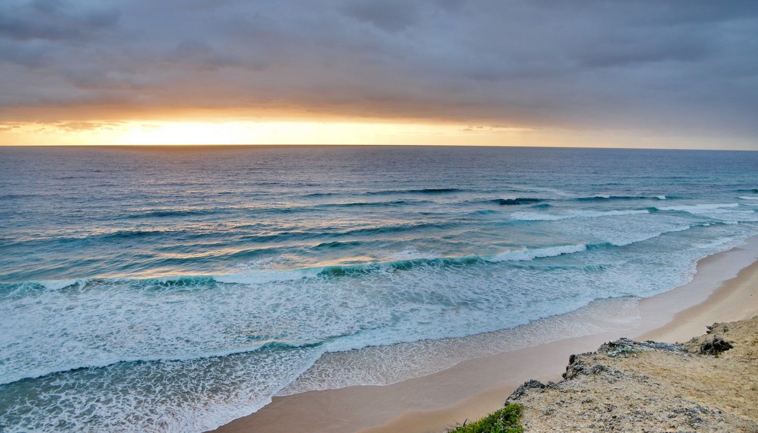 Sunset over a calm ocean with gentle waves and a sandy beach