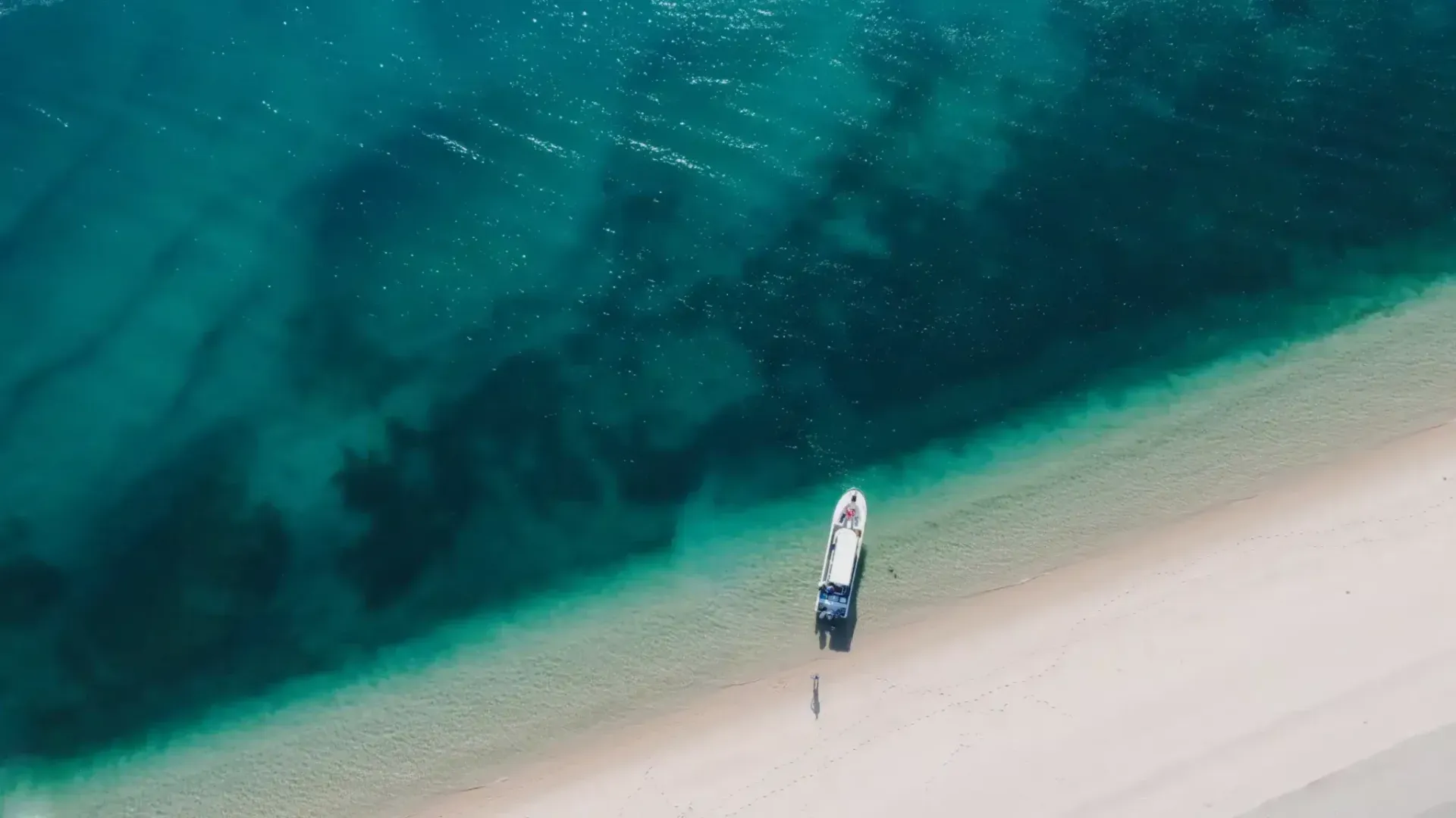 Aerial view of a white sand spit beside vivid turquoise water with a small dock.