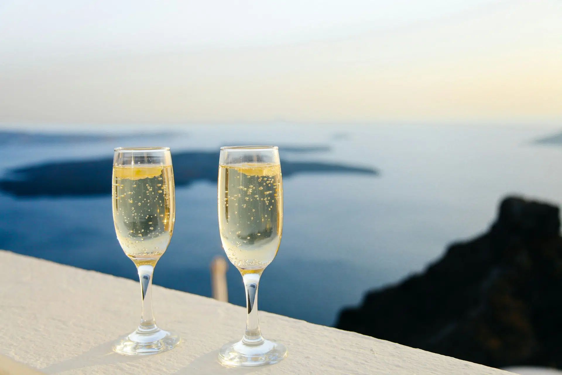 Two champagne flutes on a ledge overlooking a calm sea at sunset