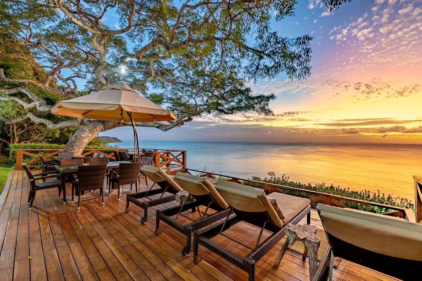 Oceanfront deck with lounge chairs, umbrella, and table at sunset over calm water