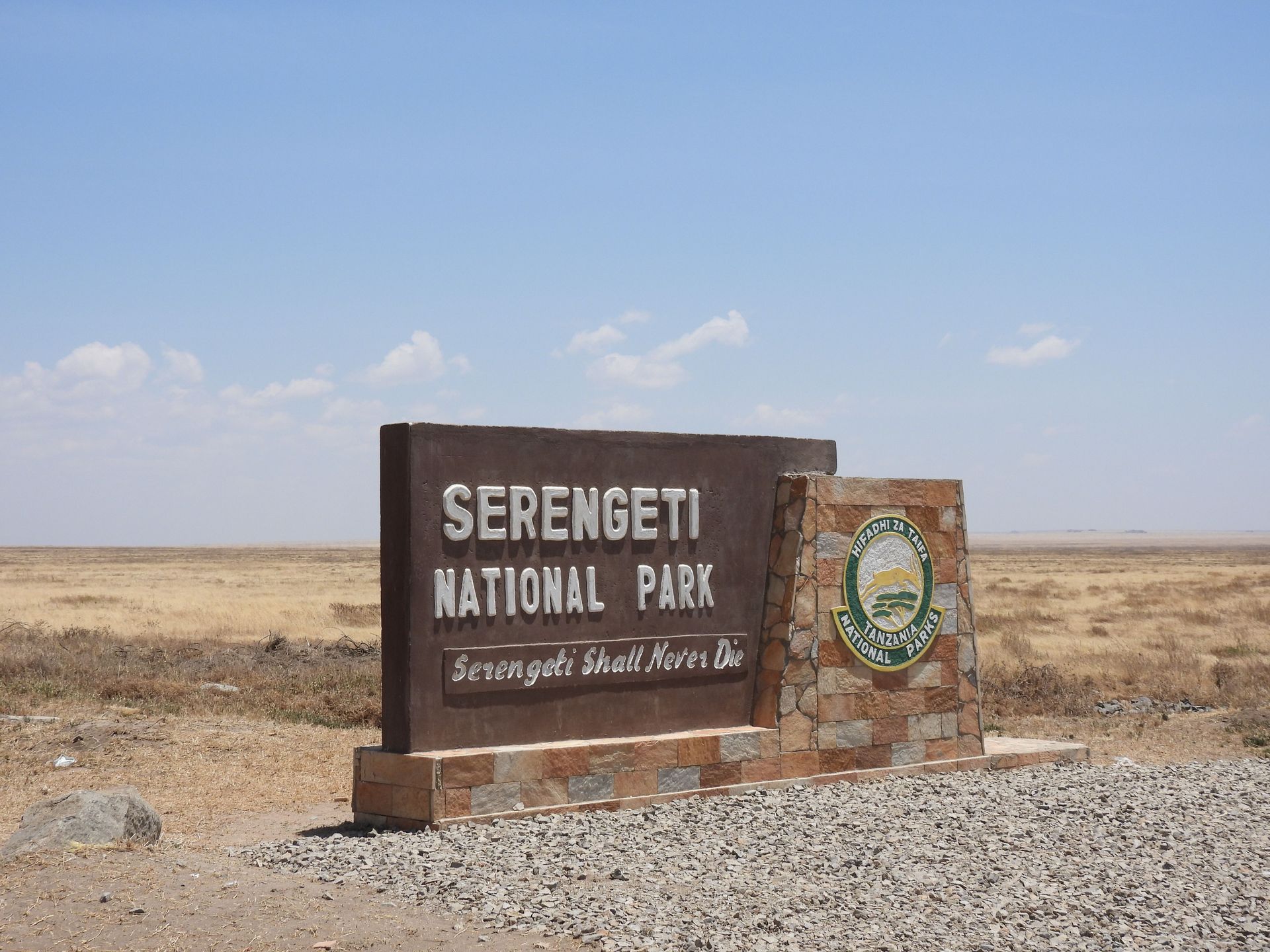 Serengeti National Park entrance sign beside a gravel road under a clear sky