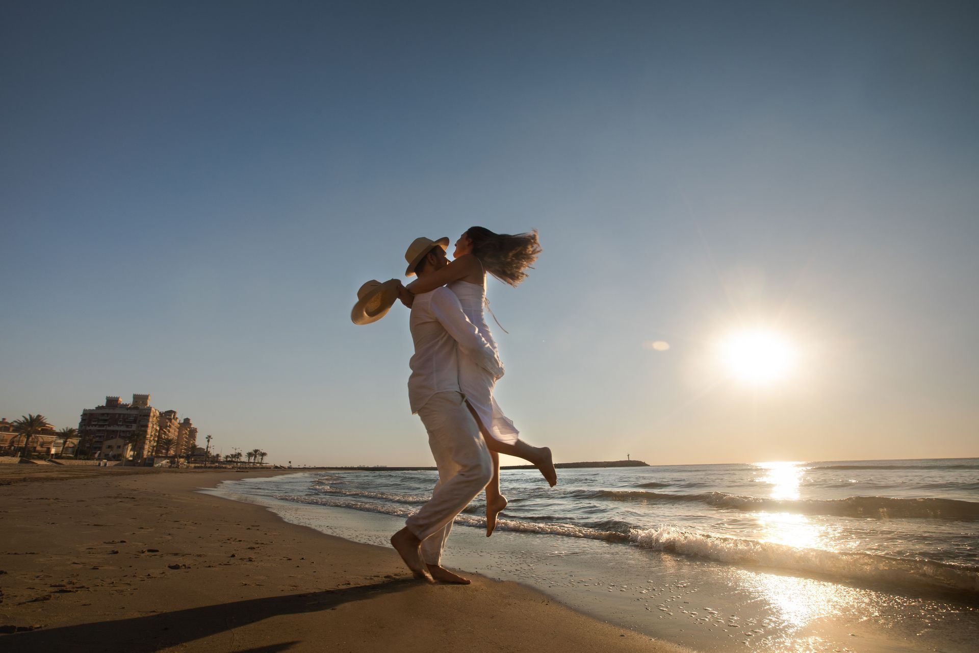Couple dancing barefoot on a beach at sunset with waves and golden light