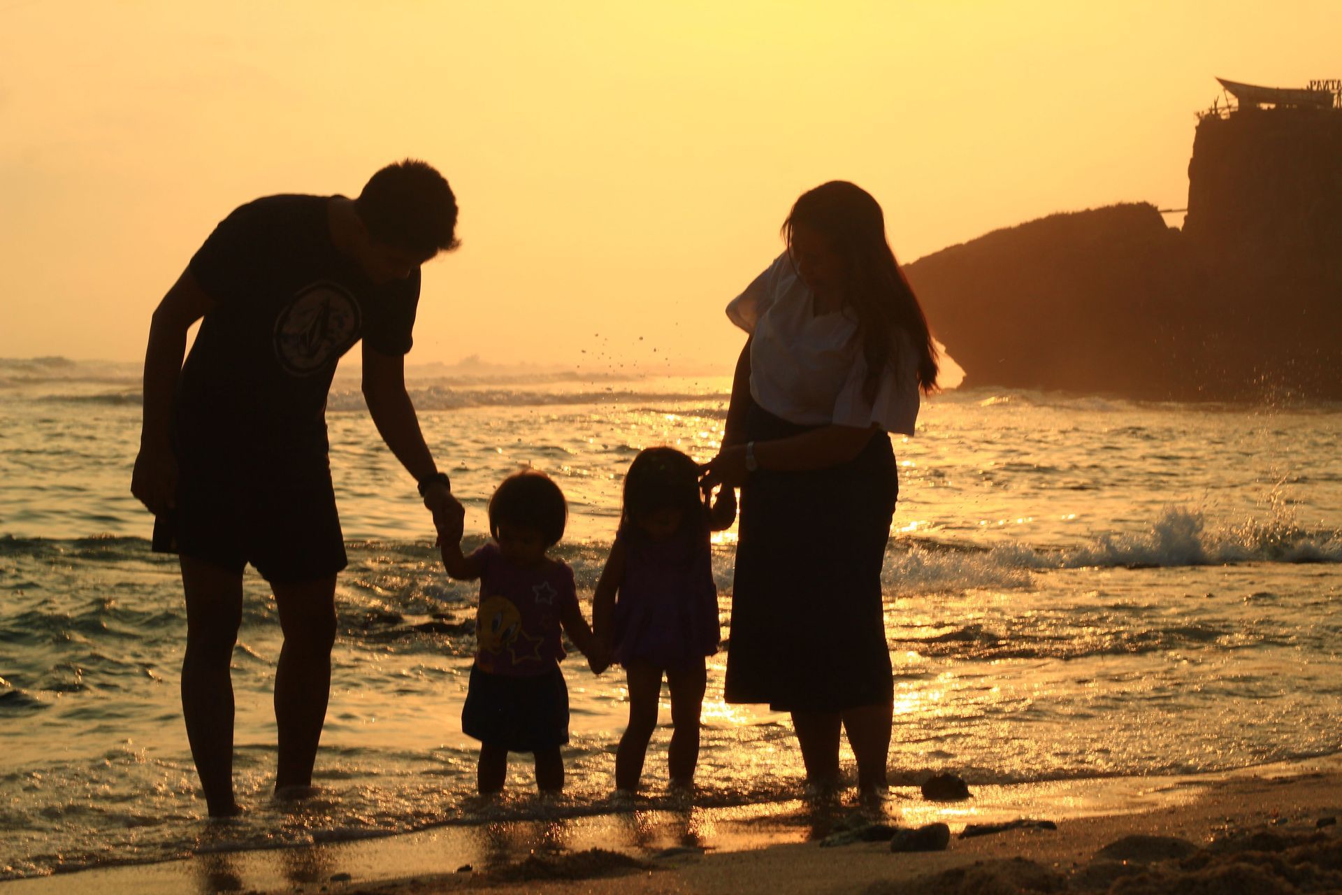 Family holding hands at the beach during sunset, with waves and cliffs in the background