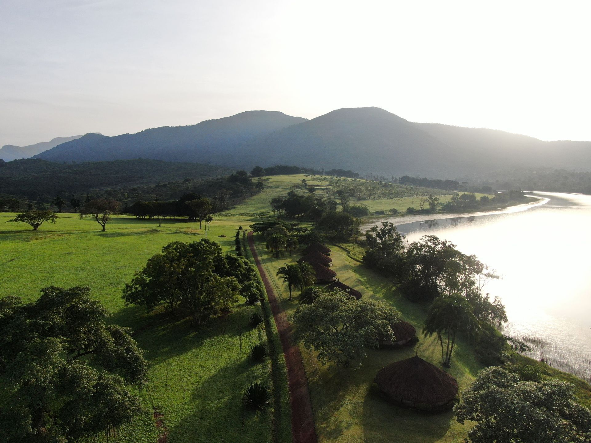 Lush green coastline with a winding path, trees, mountains, and bright water at sunset