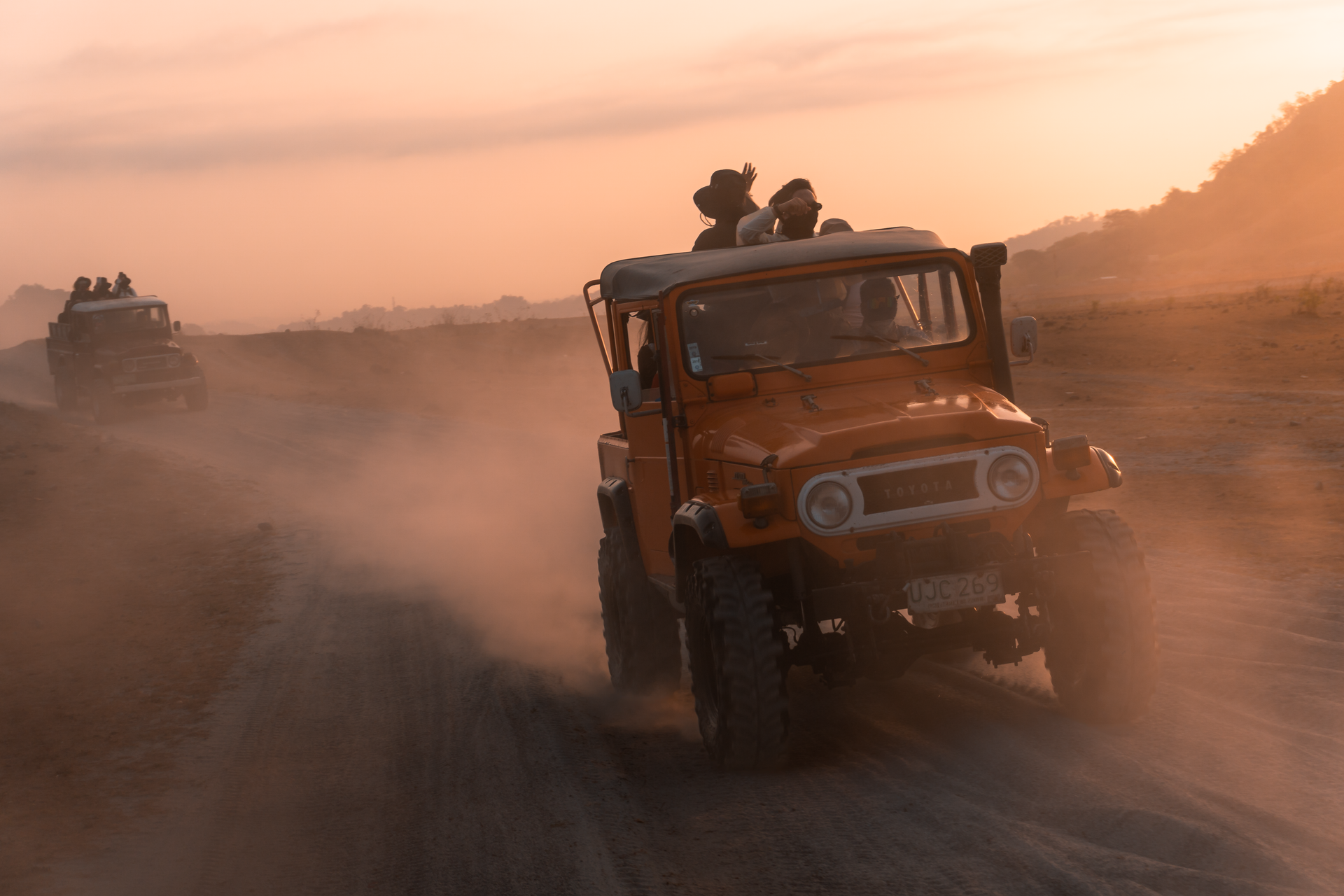 Off-road vehicle driving through dusty orange sunset on a dirt road