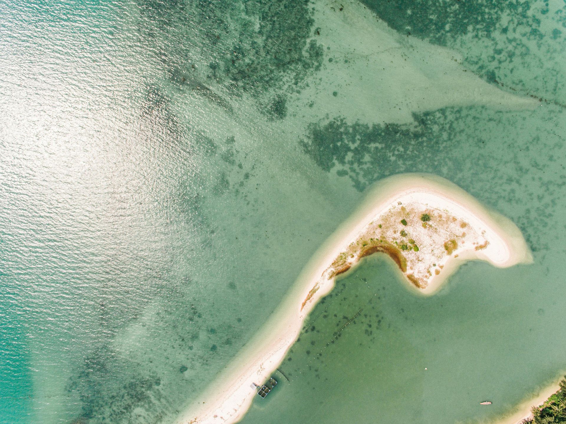 Aerial view of a white sandbar curving through green-blue water near a small sandy island