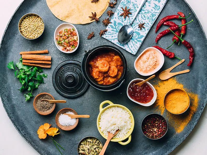 Overhead view of spices, herbs, sauces, and cooking ingredients arranged around a central pot on a dark table