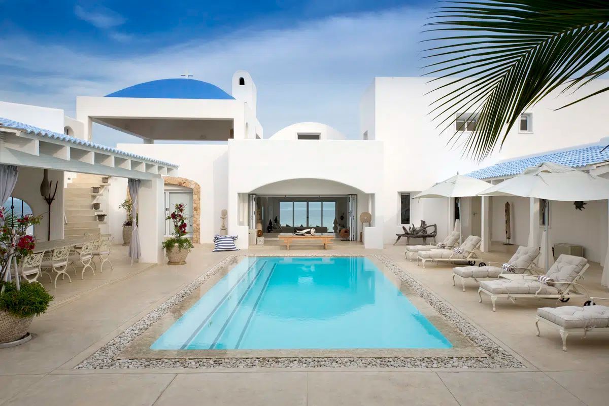 Bright white courtyard with a turquoise pool, lounge chairs, and blue-domed Mediterranean architecture