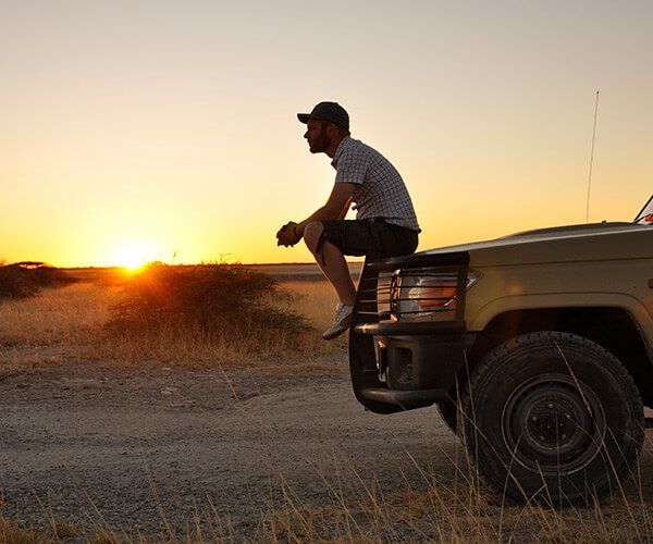 Person sitting on the front of a truck at sunset in a dry field