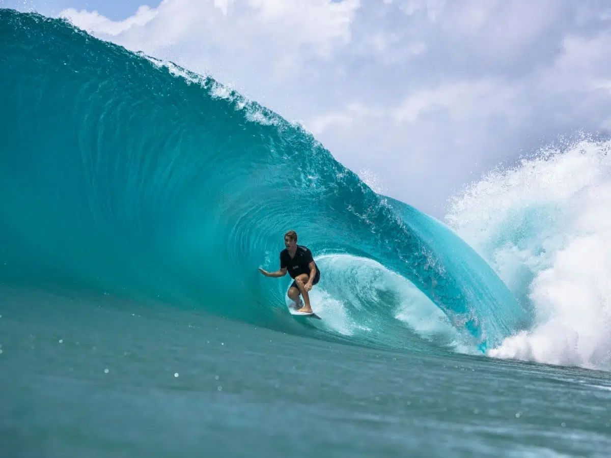 Surfer riding a turquoise wave in the ocean under a cloudy sky