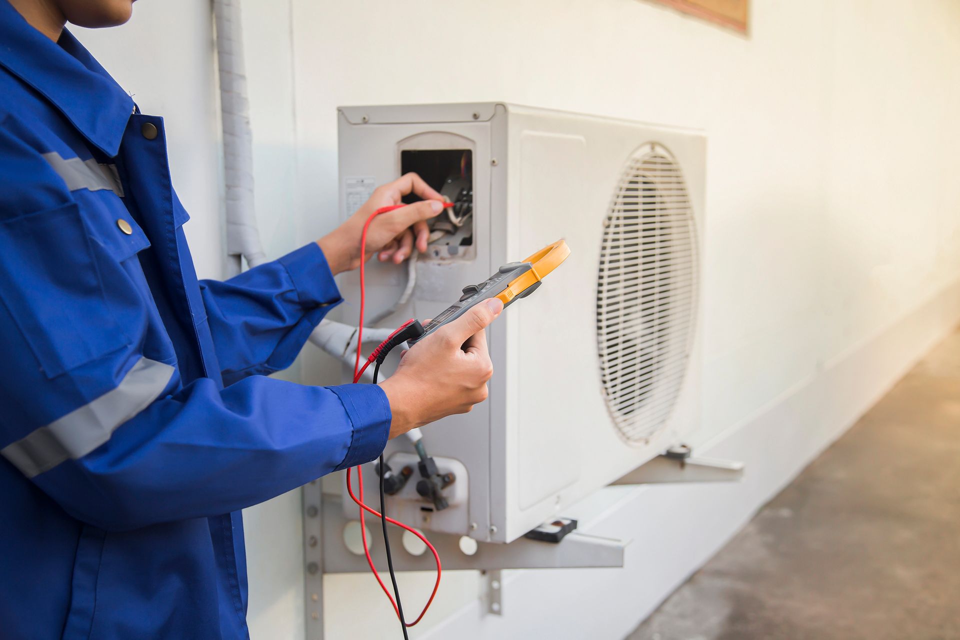 Técnico inspeccionando el cableado eléctrico dentro de una unidad exterior montada en la pared con un multímetro.