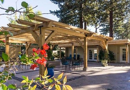 A wooden pergola with red flowers in front of a house