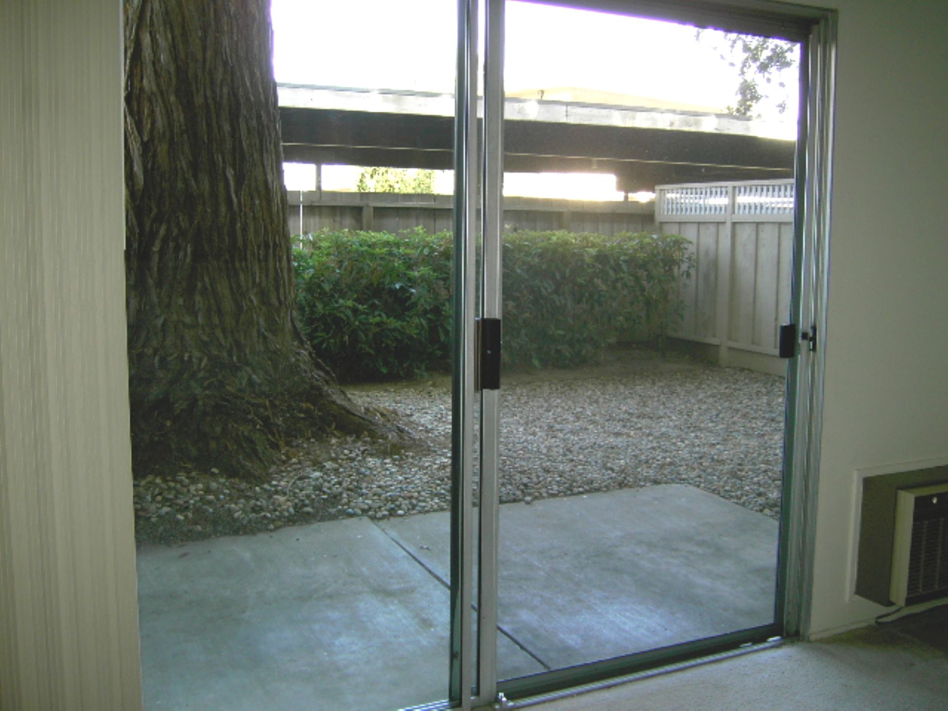 A sliding glass door leading to a patio with a tree in the background