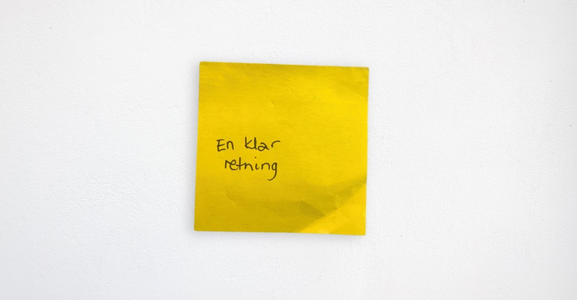 Gul Post-it lapp på hvit vegg med teksten 