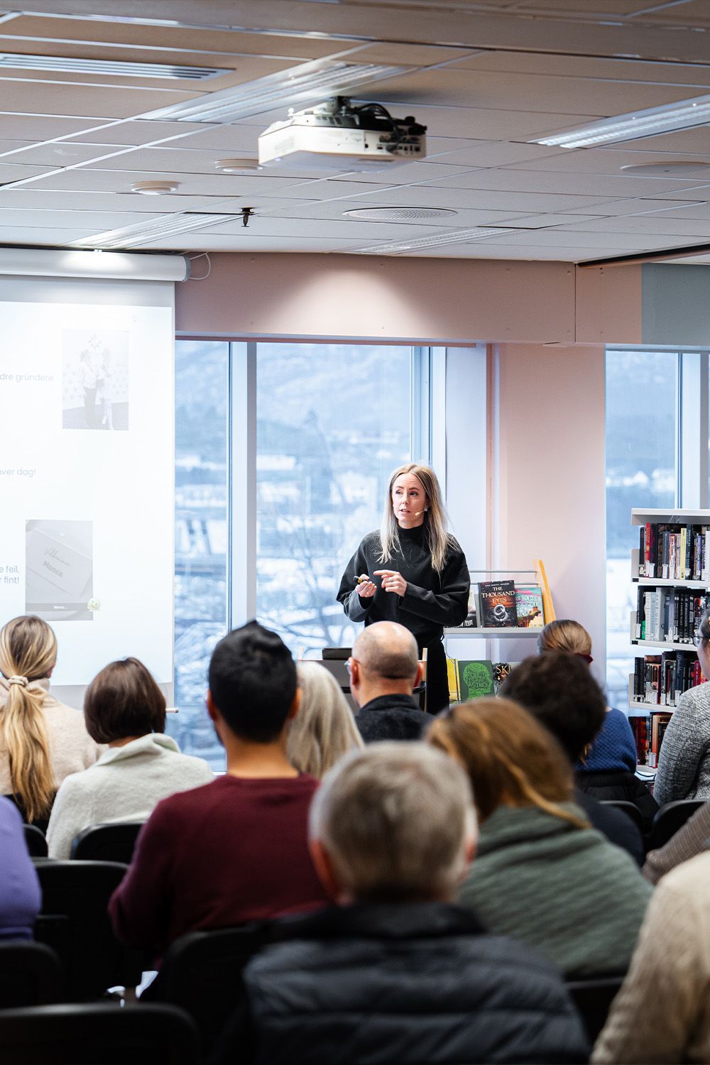 Dame står foran folkemengde og snakker i mikrofon.