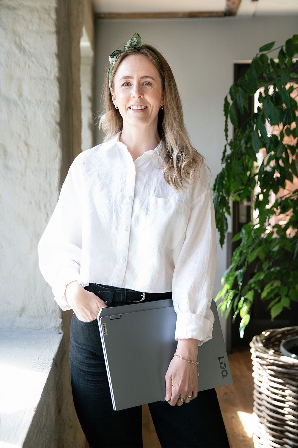 Dame i hvit skjorte holder laptop og smiler til kamera.