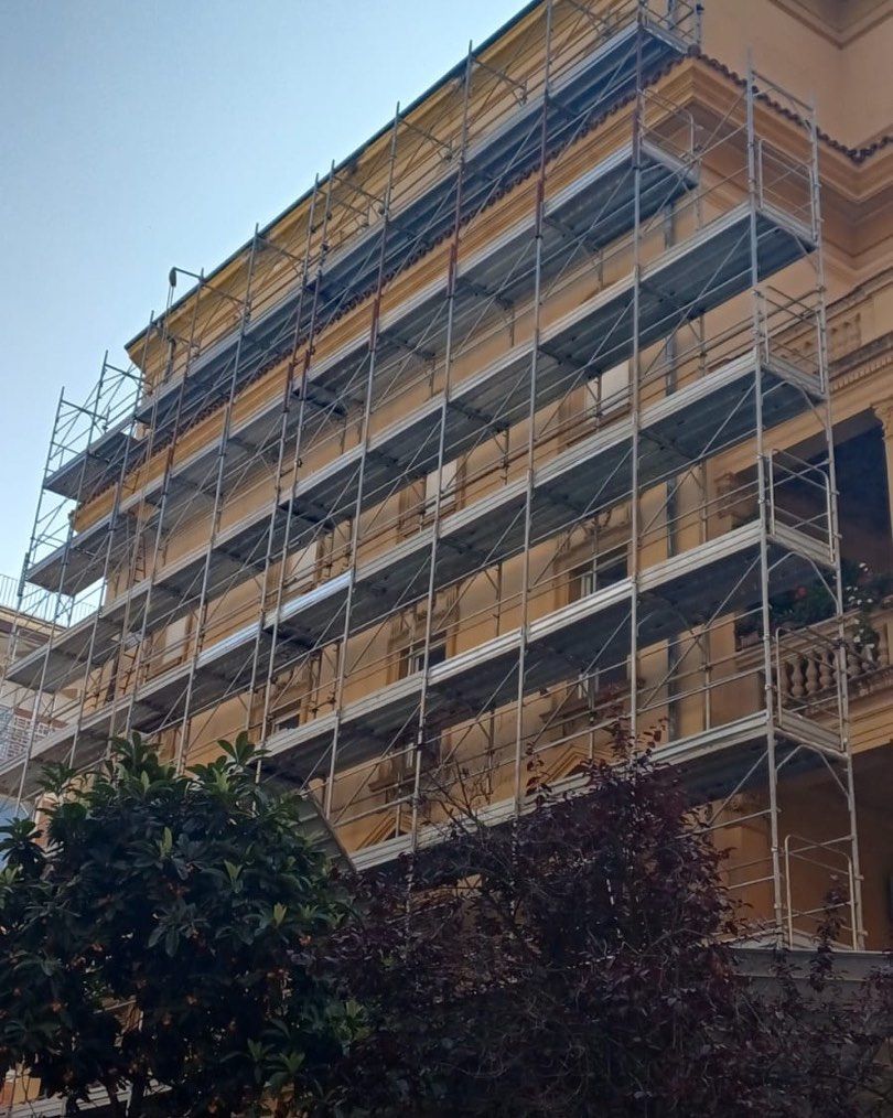 Un'impalcatura ricopre un edificio a più piani in fase di ristrutturazione, visto dal livello del suolo.