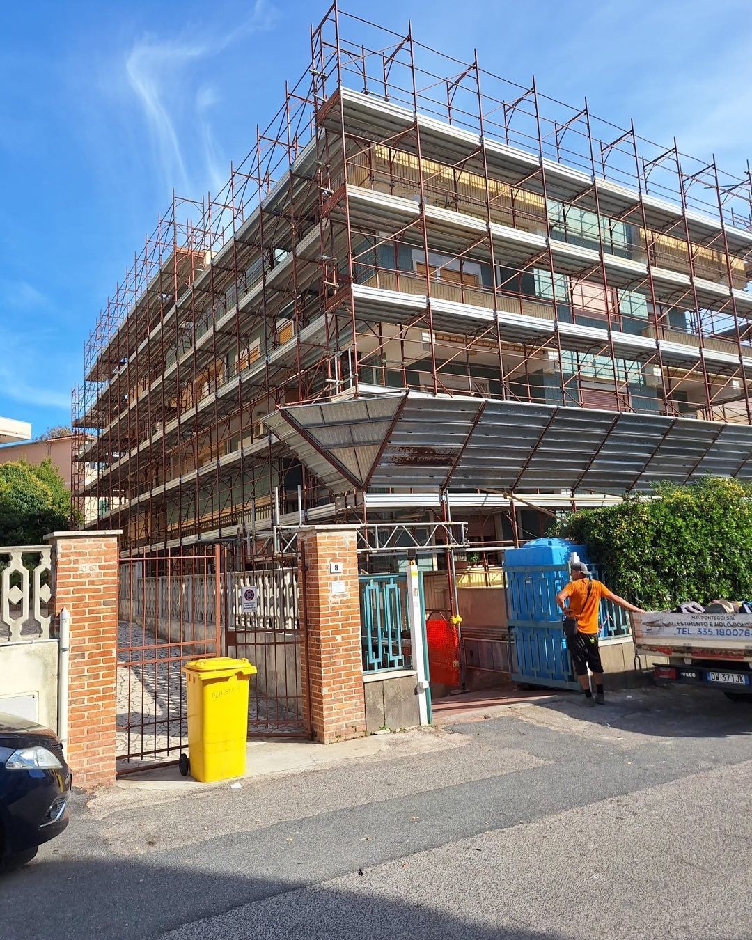 Edificio in costruzione; impalcature circondano un edificio a più piani. Una persona scarica materiali.