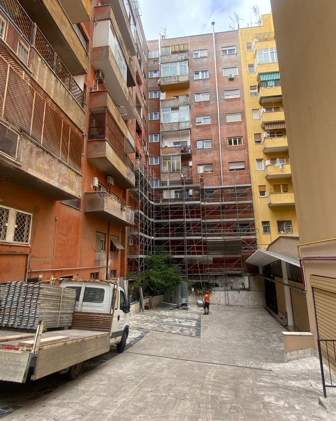 Edifici con impalcature; operaio edile, camion, mattoni e cemento in uno stretto vicolo.