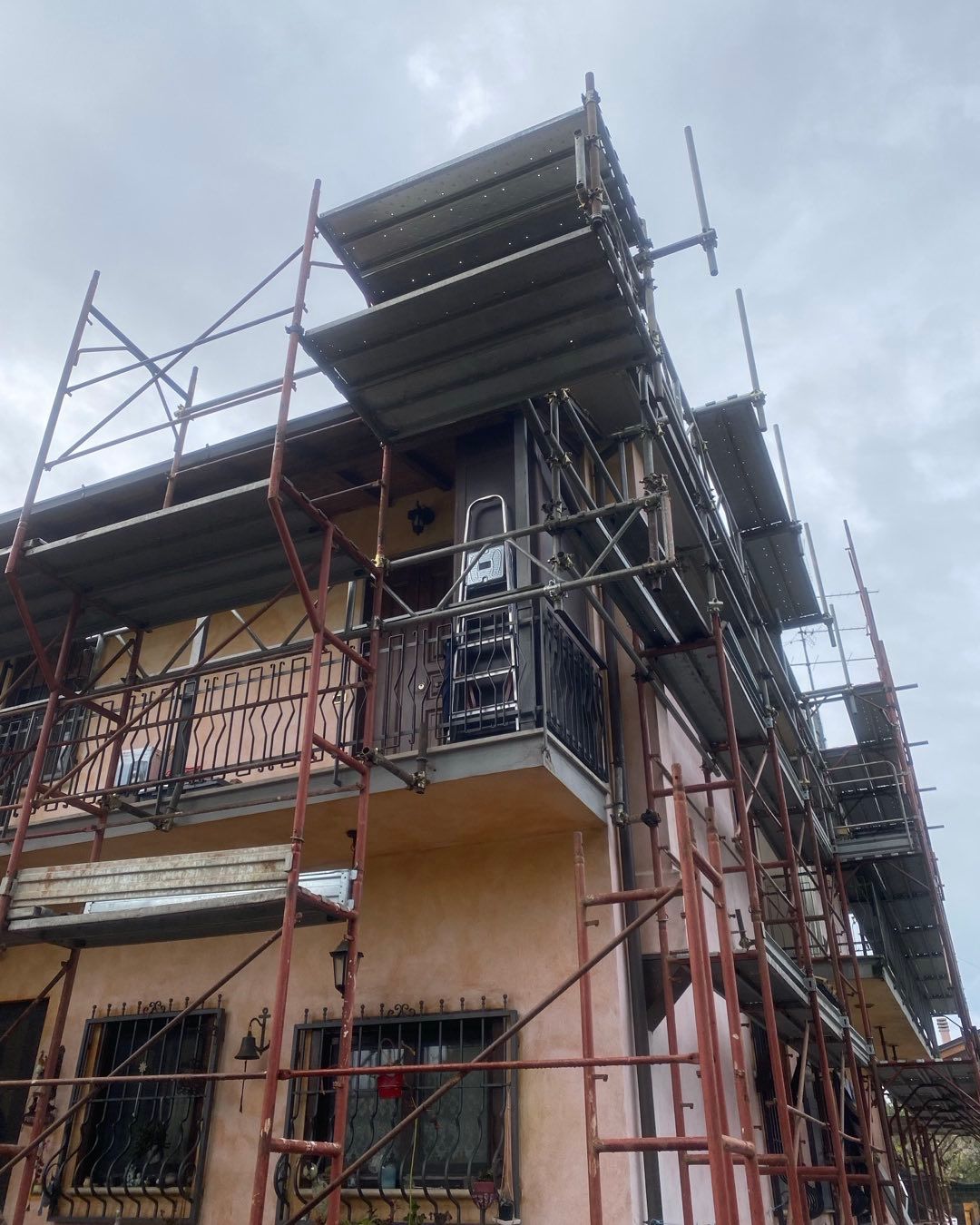 Un'impalcatura circonda un edificio a due piani in fase di ristrutturazione, cielo coperto.