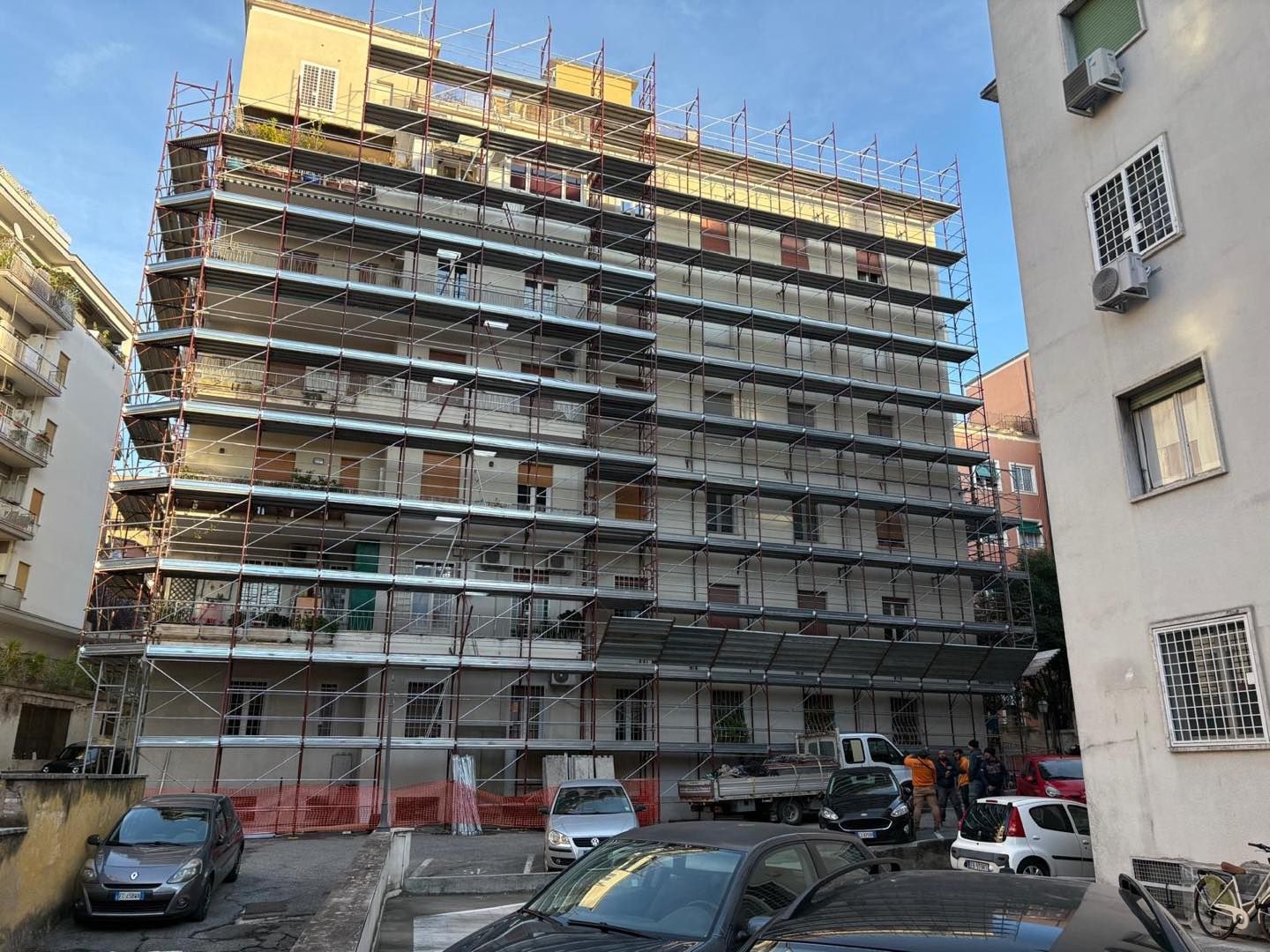 Edificio in ristrutturazione con impalcature e veicoli parcheggiati di fronte.