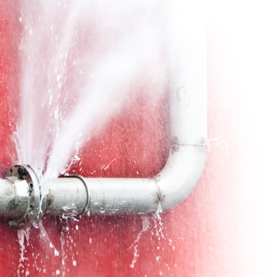 A pipe is leaking water on a red wall.