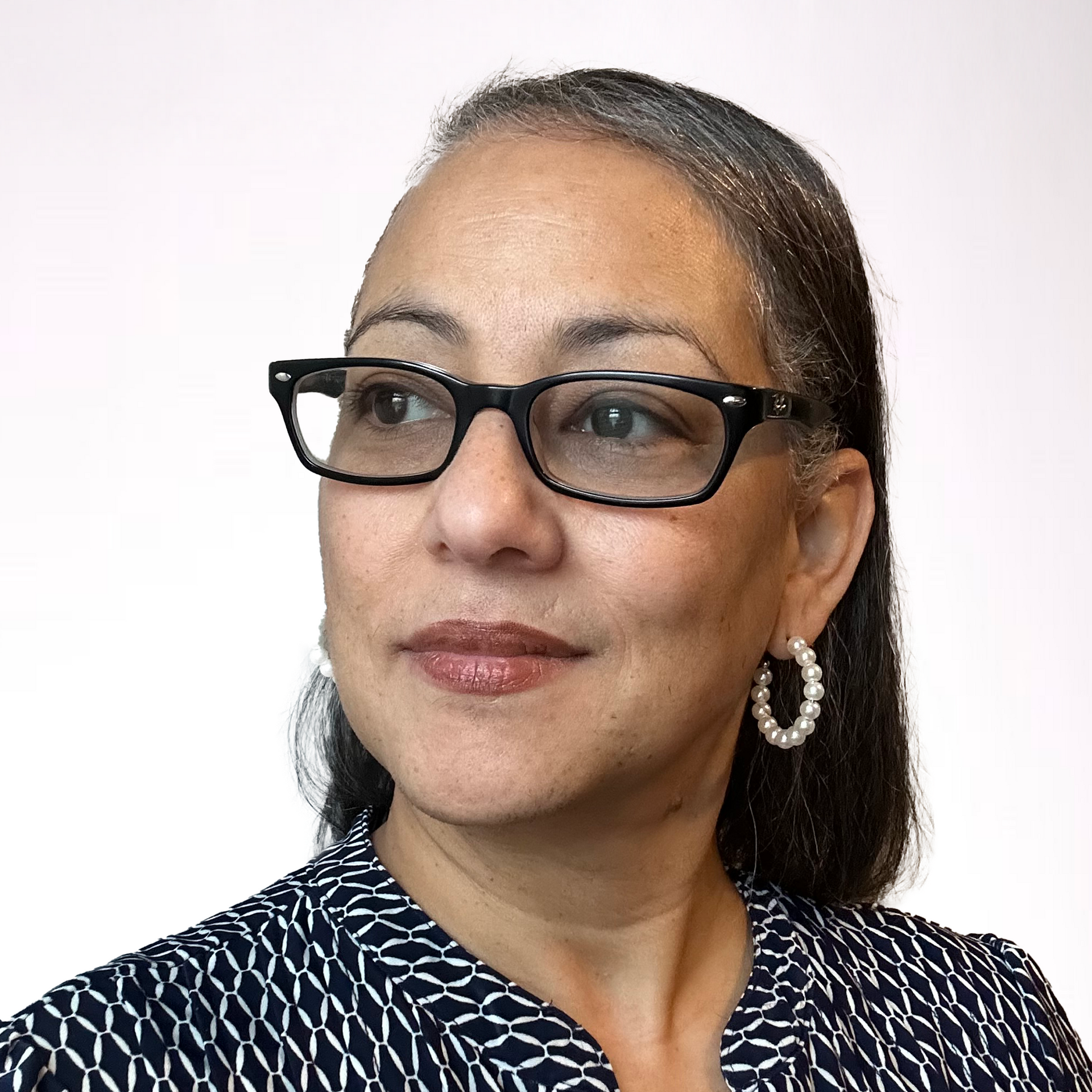A woman wearing glasses and hoop earrings is looking at the camera.