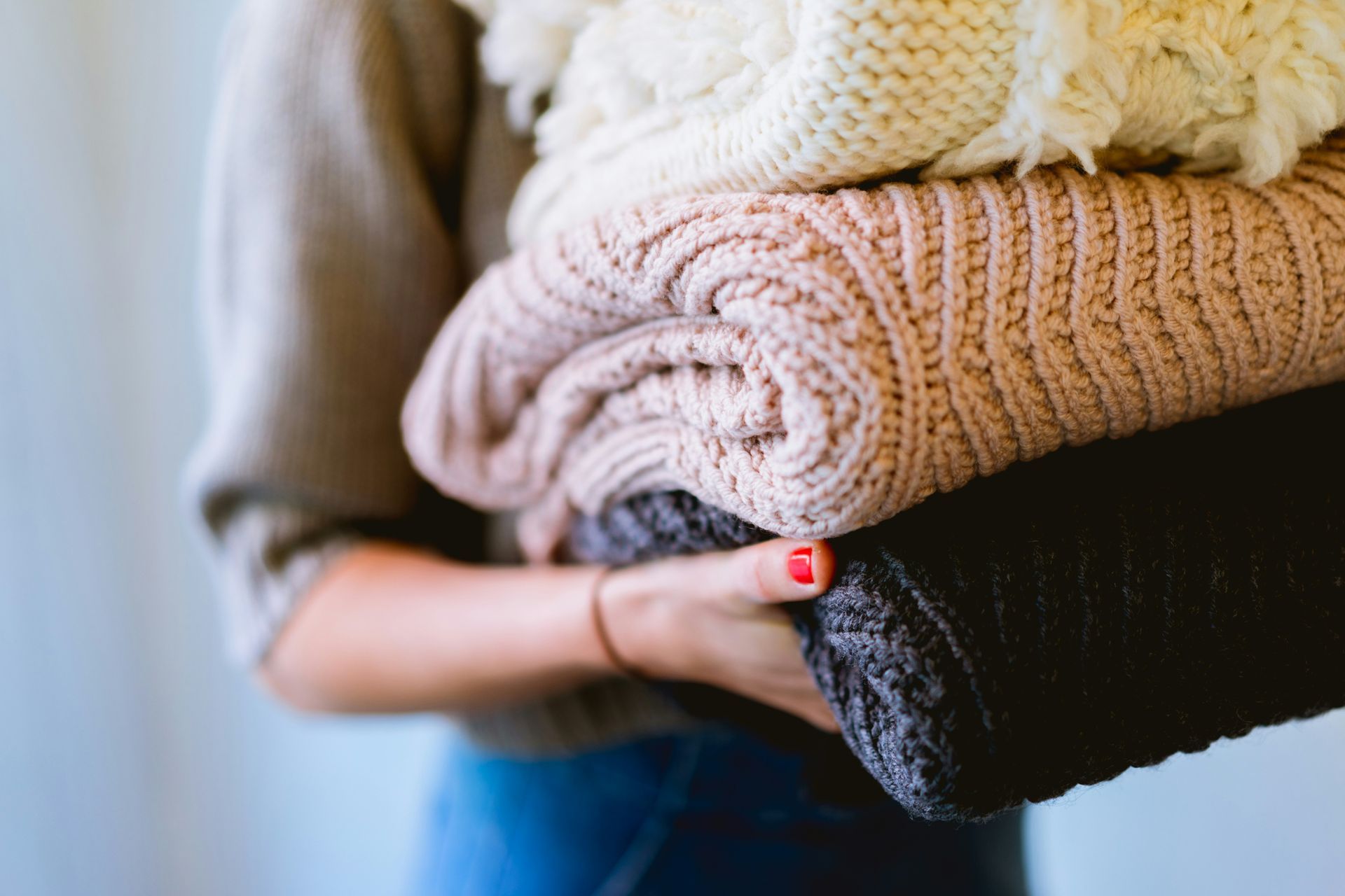 A woman is holding a pile of sweaters in her hands.