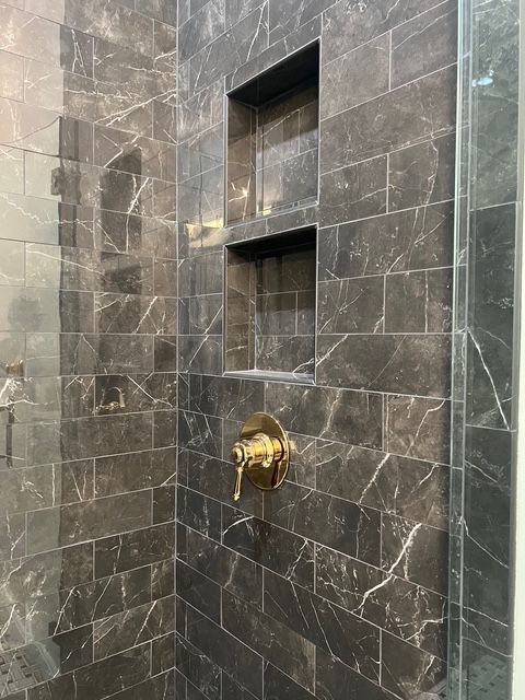 A shower wall tiled in dark marble, featuring a stacked double-recessed shelf and a gold-toned circular faucet handle.