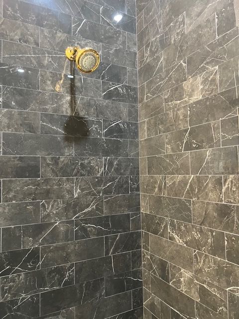 A gold shower head mounted on a wall tiled with dark grey marble featuring white veining.