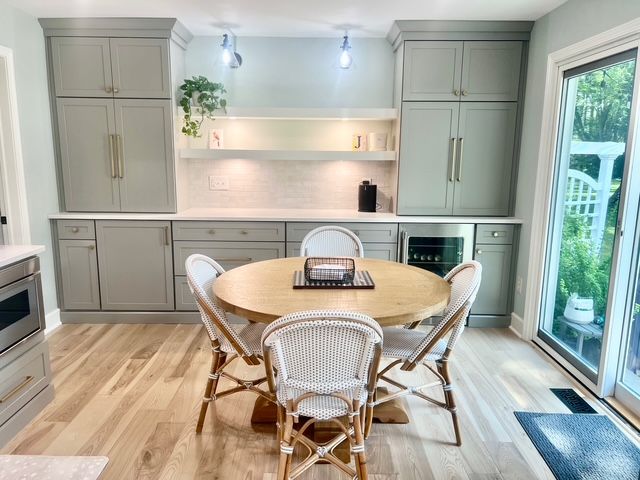 A dining area with a round wooden table, four woven chairs, light-gray cabinets, and hardwood floors. A dining area with a round wooden table, four woven chairs, light-gray cabinets, and hardwood floors.