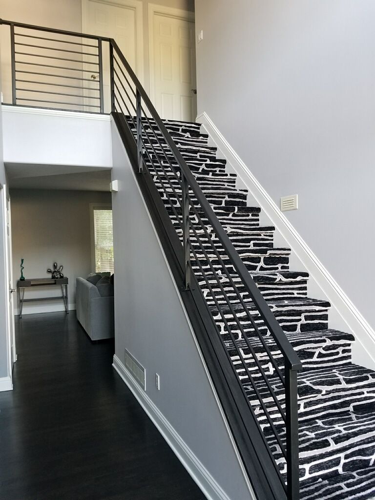 A staircase with a black-and-white patterned carpet runner and a dark metal railing, located in a modern hallway. A staircase with a black-and-white patterned carpet runner and a dark metal railing, located in a modern hallway.