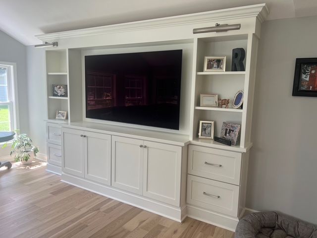 A large white built-in wall unit featuring a centered television, side shelving with decor, and lower storage cabinets.