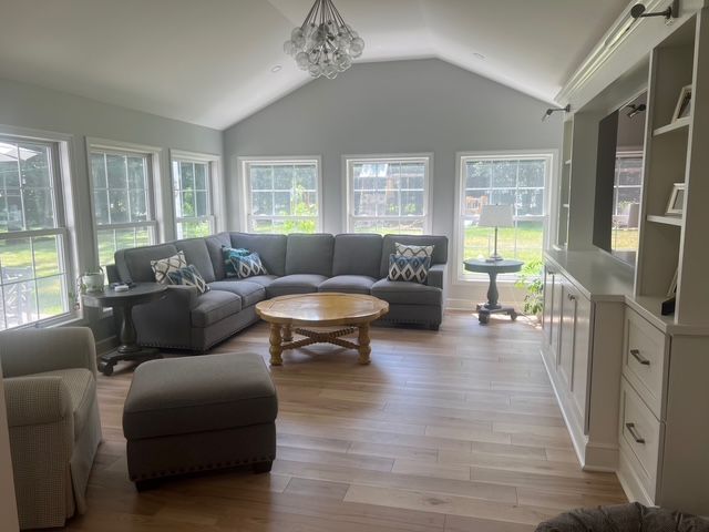 A sunlit living room with a large gray sectional sofa, round wooden coffee table, ottoman, and built-in white cabinets. A sunlit living room with a large gray sectional sofa, round wooden coffee table, ottoman, and built-in white cabinets.