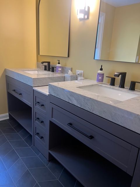 Modern double vanity with gray cabinets, marble countertops, black fixtures, and framed mirrors in a bathroom.