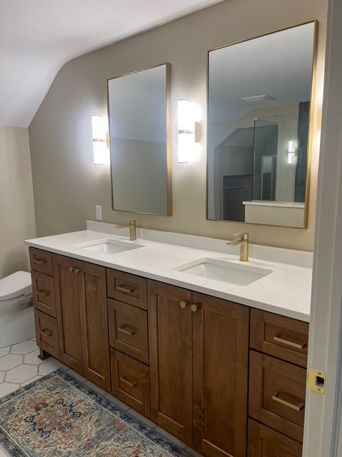 A double bathroom vanity with wood cabinets, gold hardware, white countertops, dual sinks, and rectangular mirrors.