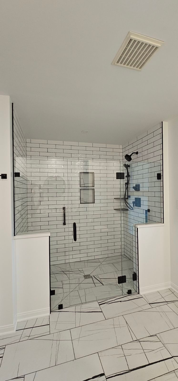 A walk-in shower with white brick-patterned walls and marble-style tile floor, enclosed by a frameless glass door. A walk-in shower with white brick-patterned walls and marble-style tile floor, enclosed by a frameless glass door.