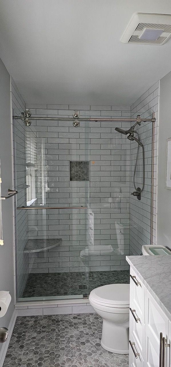 A renovated bathroom featuring a glass shower with white subway tiles and gray pebble floor tiling, next to a white toilet. A renovated bathroom featuring a glass shower with white subway tiles and gray pebble floor tiling, next to a white toilet.