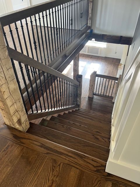 A high-angle view down dark wooden stairs with black metal railings, leading into a bright, open lower-level living area.